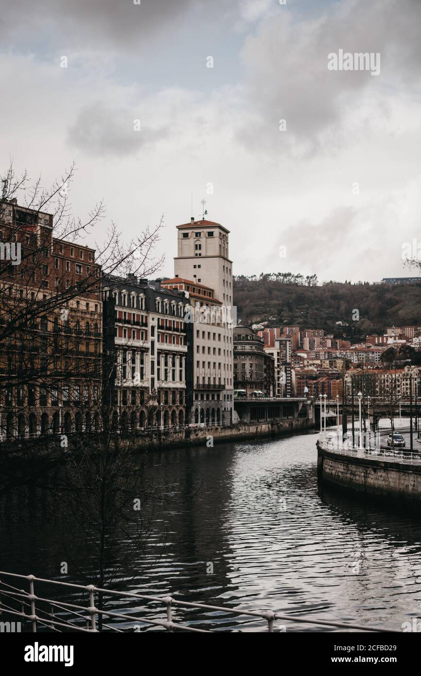 Gray clouds floating on sky over beautiful old buildings and canal with rippled water on dull day in Bilbao, Spain Stock Photo