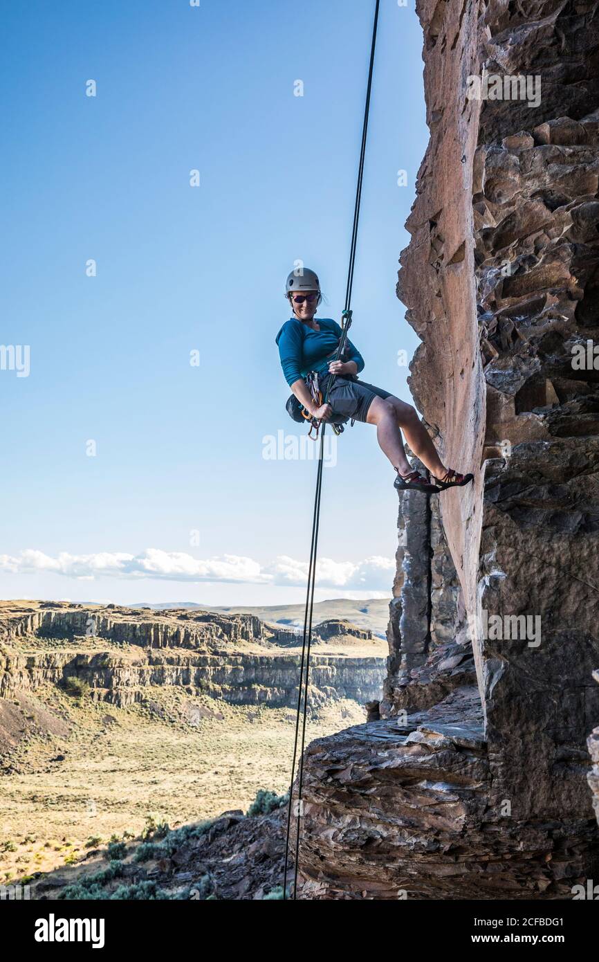 A middle aged woman rappelling from a rock climb in Echo Basin near Frenchmans Coulee, Eastern Washington, USA. Stock Photo