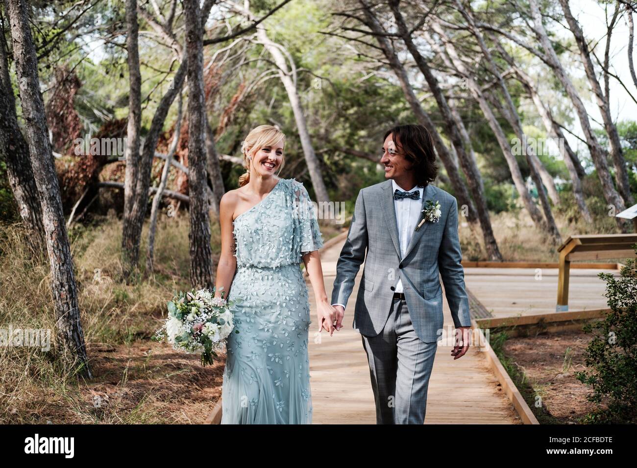 Young newly wedded couple in wedding wear walking holding hands on ...