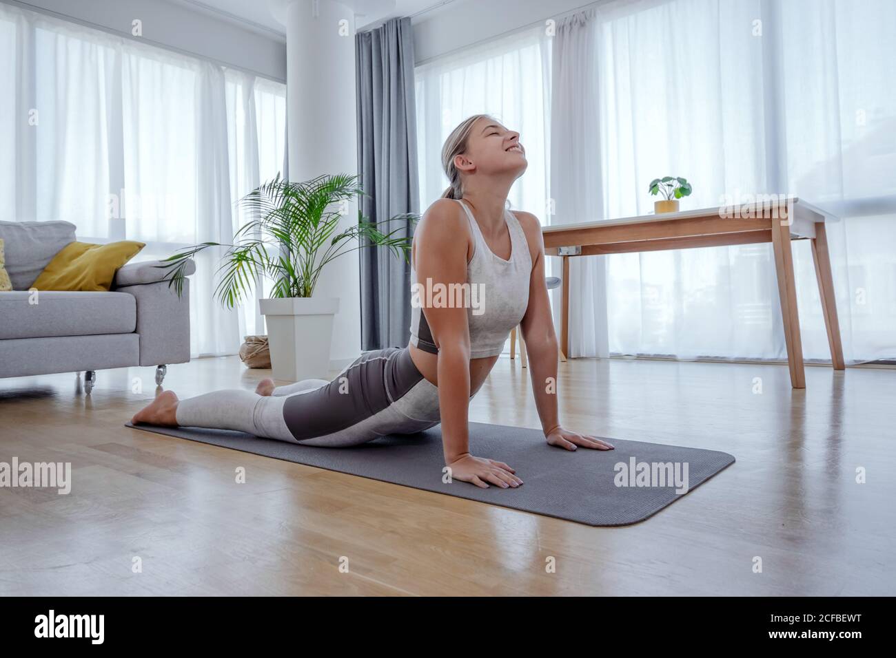 Beautiful active young woman practices yoga asana upward facing dog pose at home. Healthy lifestyle and sports concept. Series of exercise poses. Stock Photo