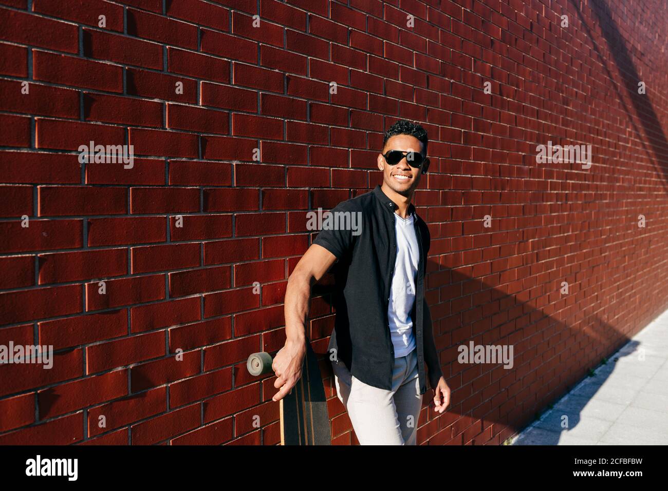 Young black male with long board leaning on wall Stock Photo