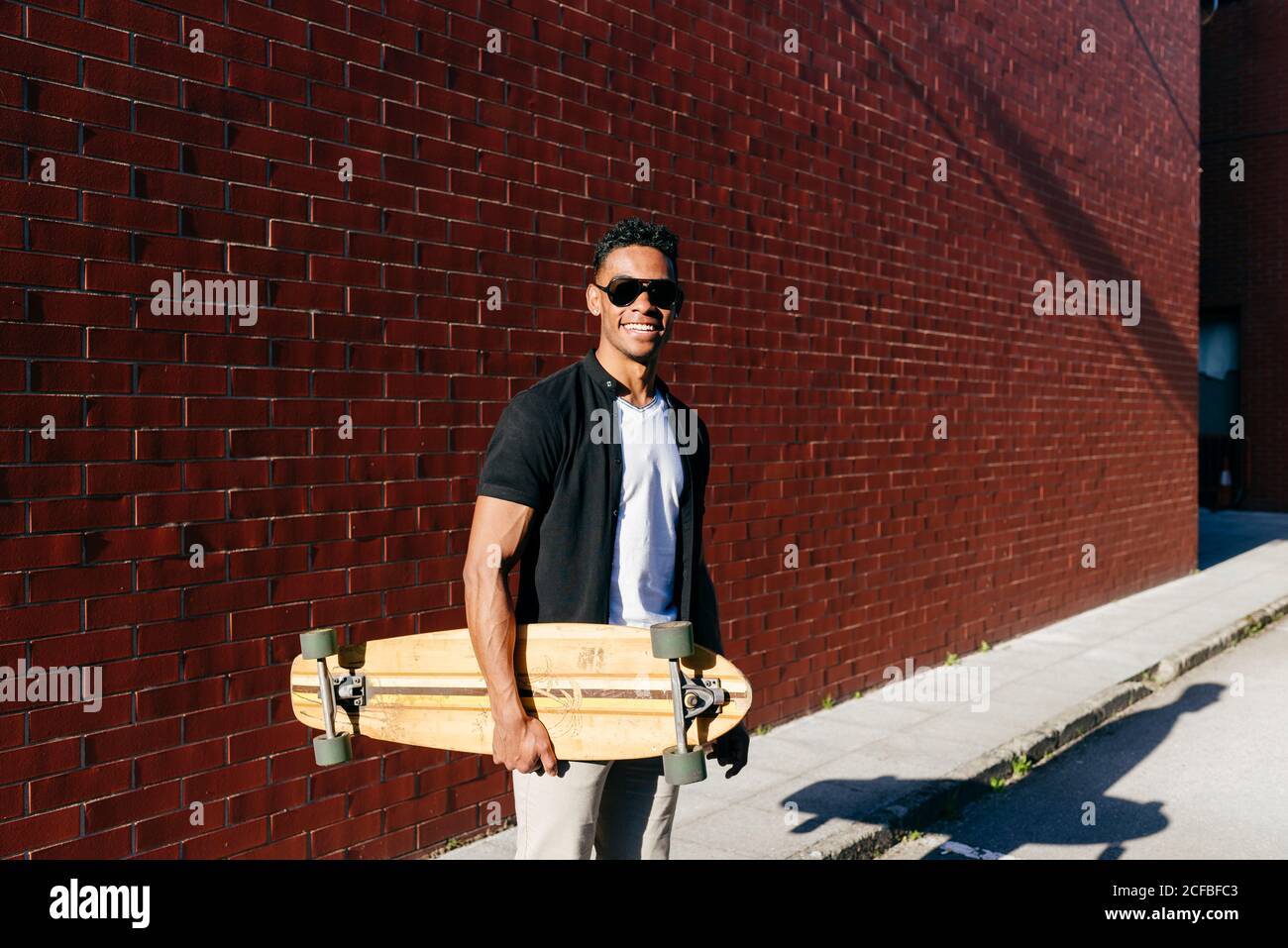 Young black male with long board standing near wall Stock Photo