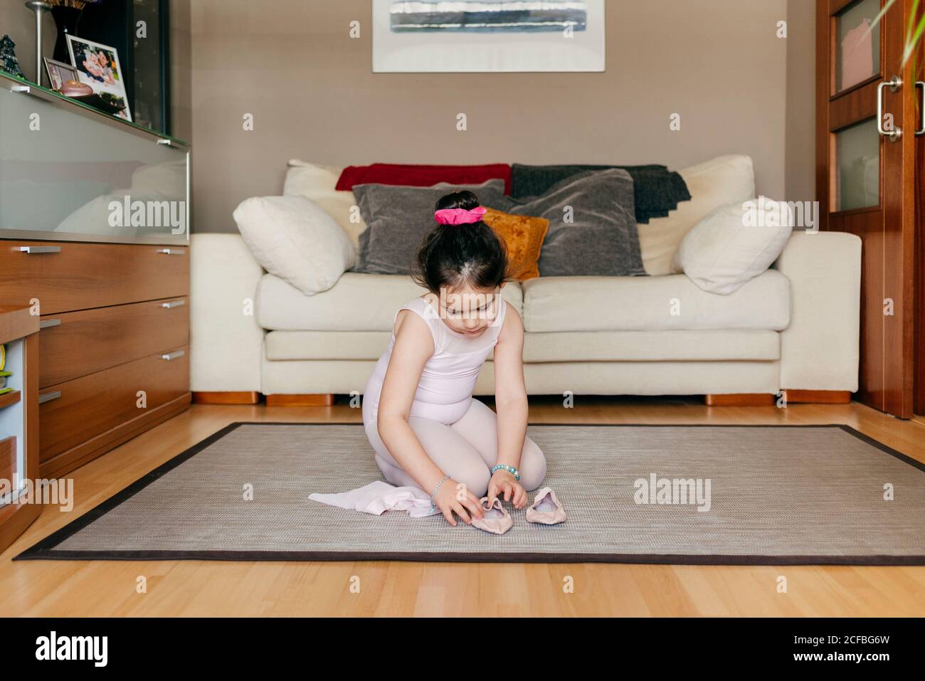 https://c8.alamy.com/comp/2CFBG6W/cute-girl-in-leotard-and-tights-sitting-on-floor-near-sofa-and-putting-on-dance-shoes-before-ballet-rehearsal-at-home-2CFBG6W.jpg