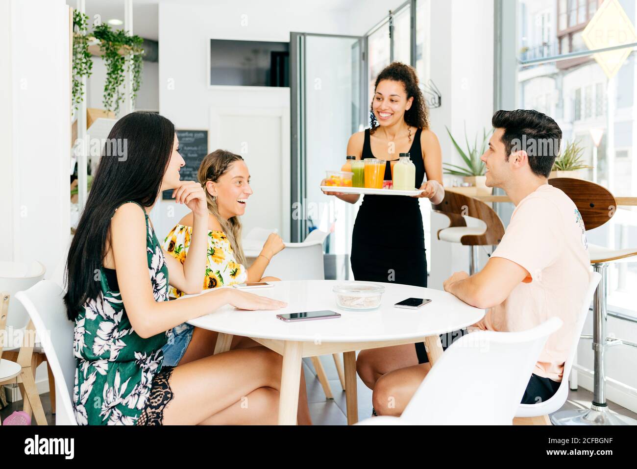 Cheerful waitress serving healthy drinks for friends Stock Photo