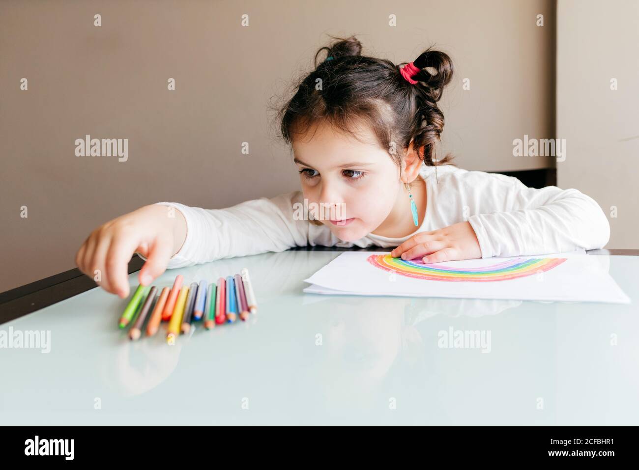 https://c8.alamy.com/comp/2CFBHR1/concentrated-little-girl-in-casual-clothes-sitting-at-wooden-table-and-taking-colored-pencil-while-drawing-rainbow-on-paper-at-home-2CFBHR1.jpg