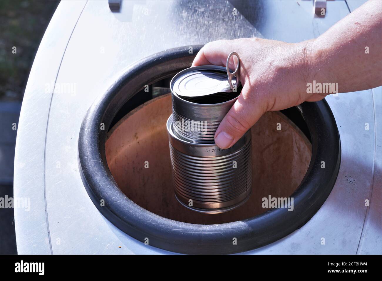 A man dropping empty cans into container for separation of home waste. A sign of awareness concerning environment, waste management, climate. Stock Photo