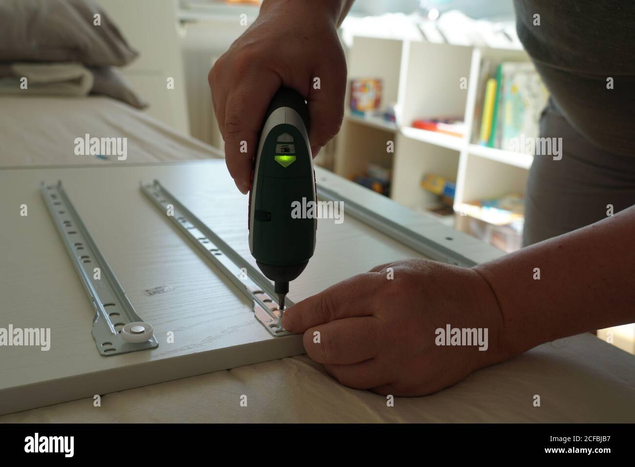 A man assembling a drawer of a computer desk for his son in his room using power cordless screwdriver close-up. He is using a tool and instructions. Stock Photo