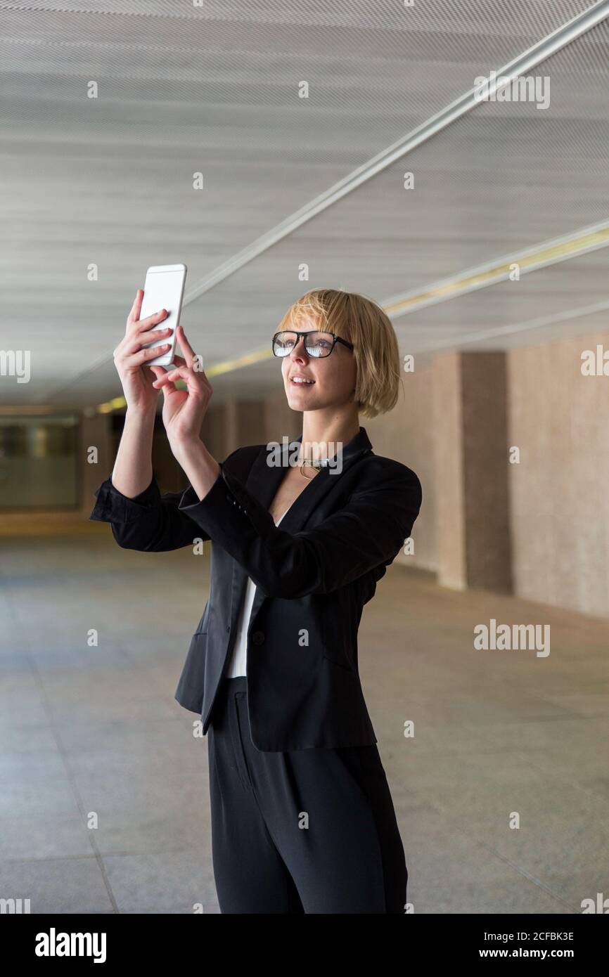 Blonde businessWoman in formal clothes taking selfie or browsing smartphone in big hall Stock Photo