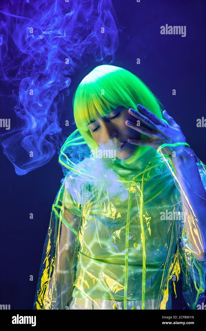 Young pretty unusual Asian Woman in plastic transparent raincoat and yellow hair smoking in fluorescent light Stock Photo Alamy
