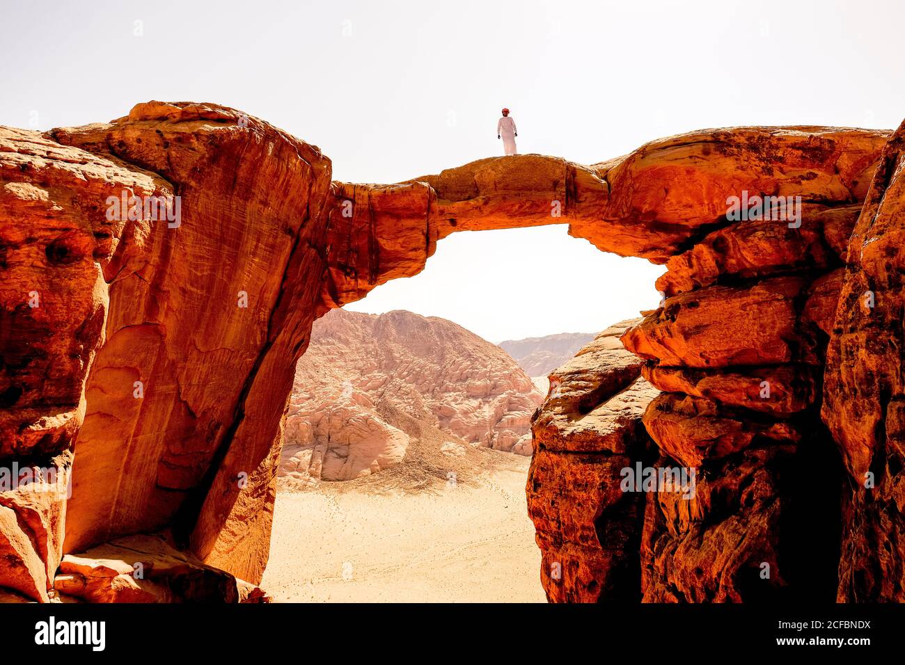 A Bedouin man stands atop a rock arch in Wadi Rum, Jordan Stock Photo