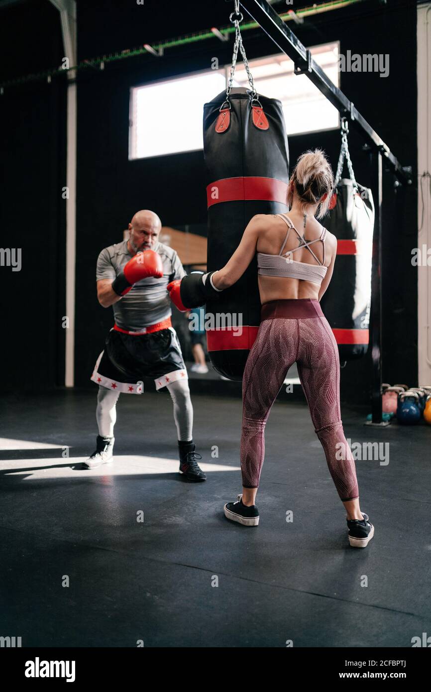 Back view of strong anonymous female athlete in boxing gloves holding
