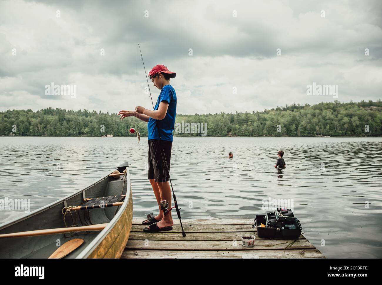 Teen boy fishing from a dock on a lake with brothers swimming nearby