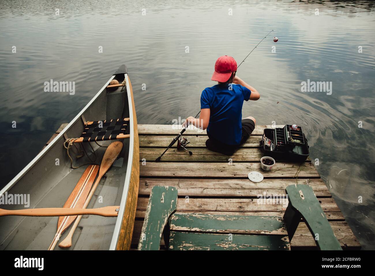 Teen boy fishing from a dock on a lake with tackle box in the summer Stock  Photo - Alamy