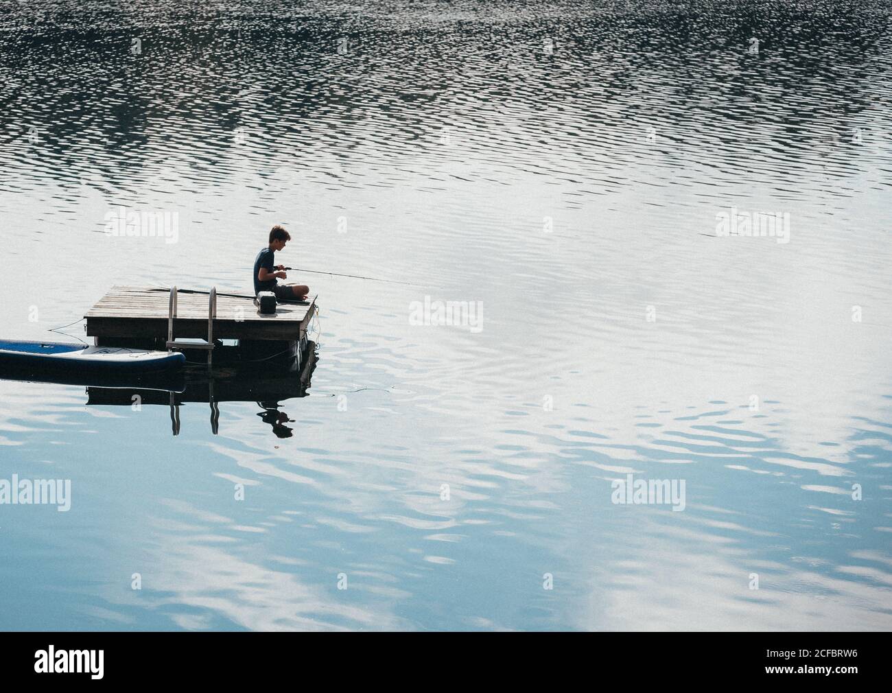 Teen boy fishing from a swim platform on a lake in the summer Stock