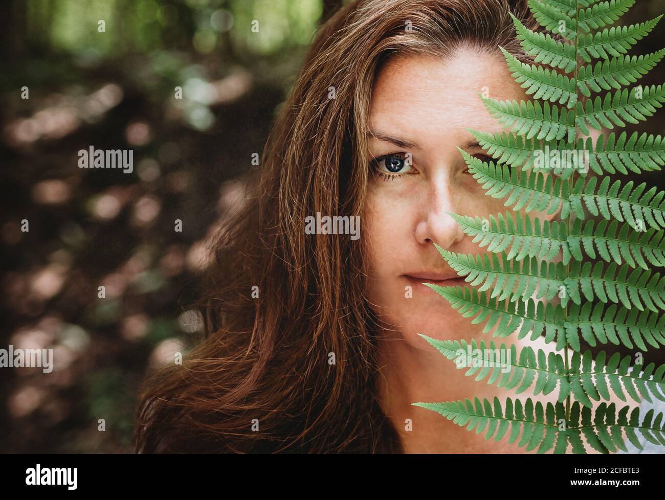 Portrait of a brunette woman covering half her face with a fern leaf ...