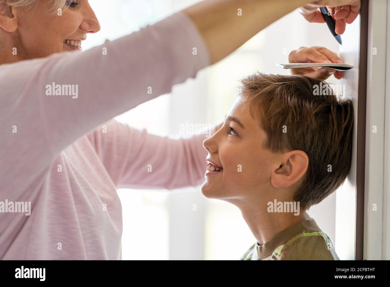 Mother measuring the height of her son against wall at home Stock Photo