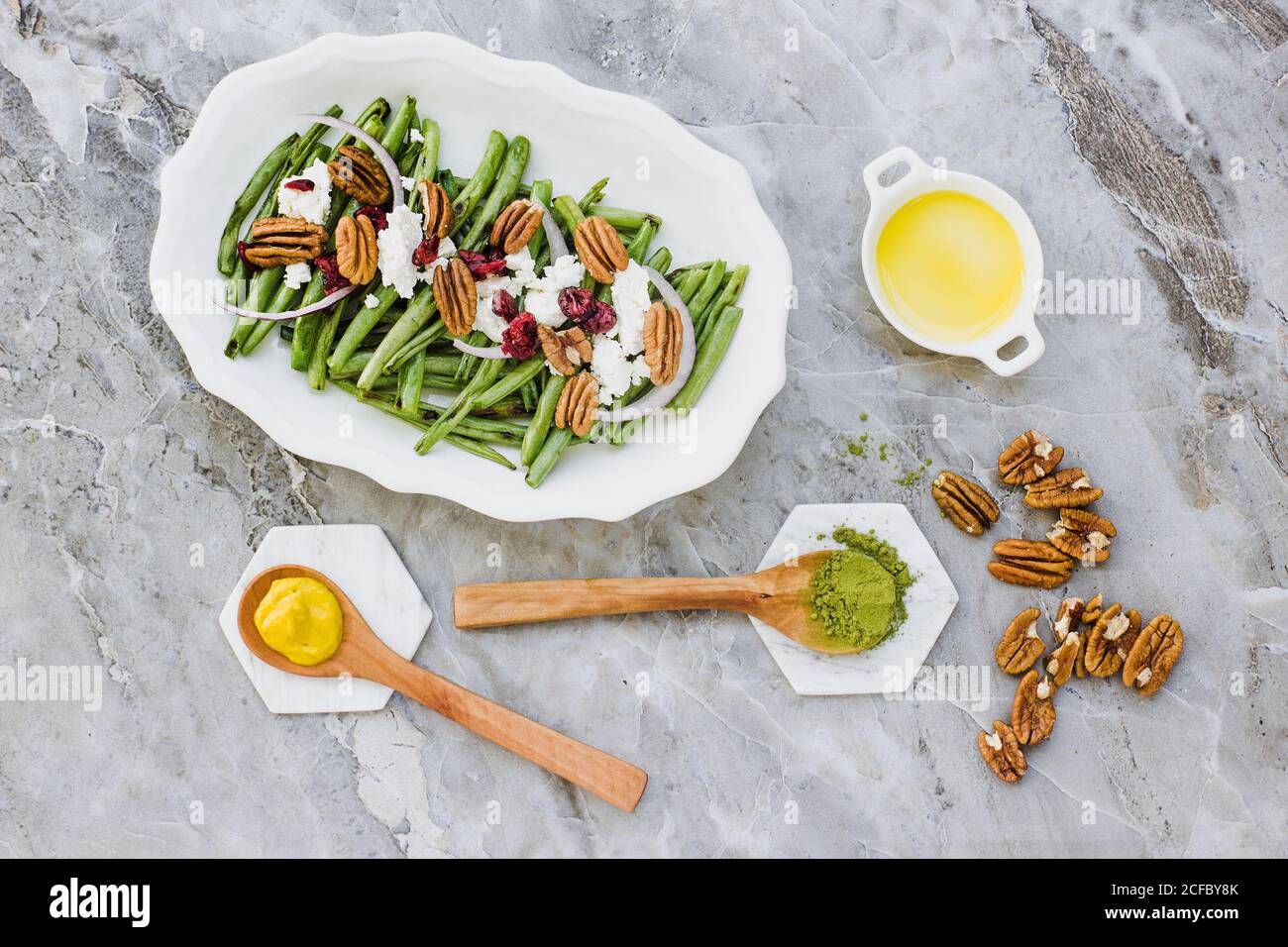 From above of oval plate with salad of green beans topped with goat cheese and pecan nuts on marble surface with dressing ingredients Stock Photo