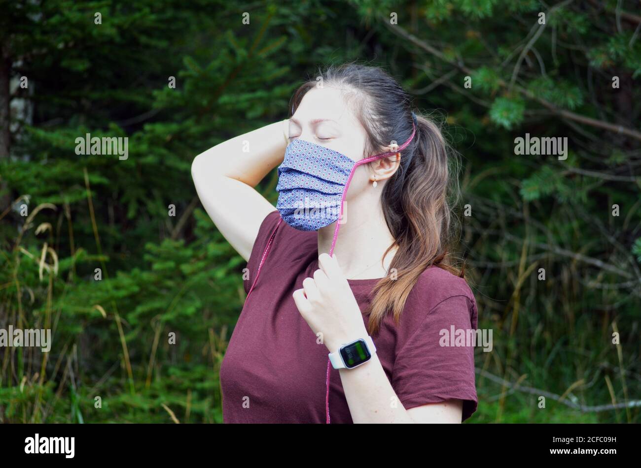 Portrait of young woman with brown hair ponytail in a colorful patterned face mask on a nature background Stock Photo