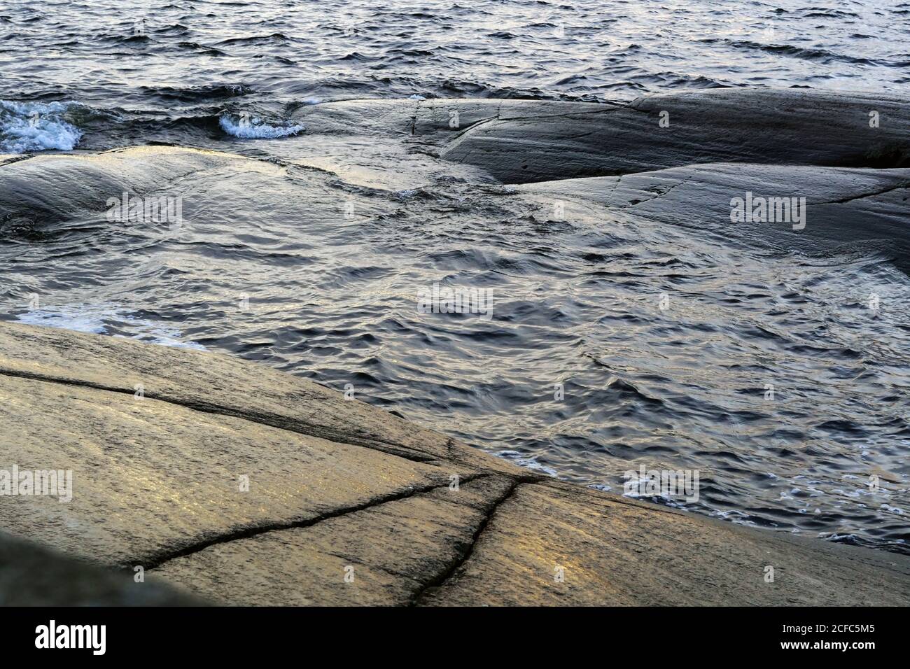 From above dark rippled ocean waves dashing slowly against smooth rocks at seaside in twilight Stock Photo