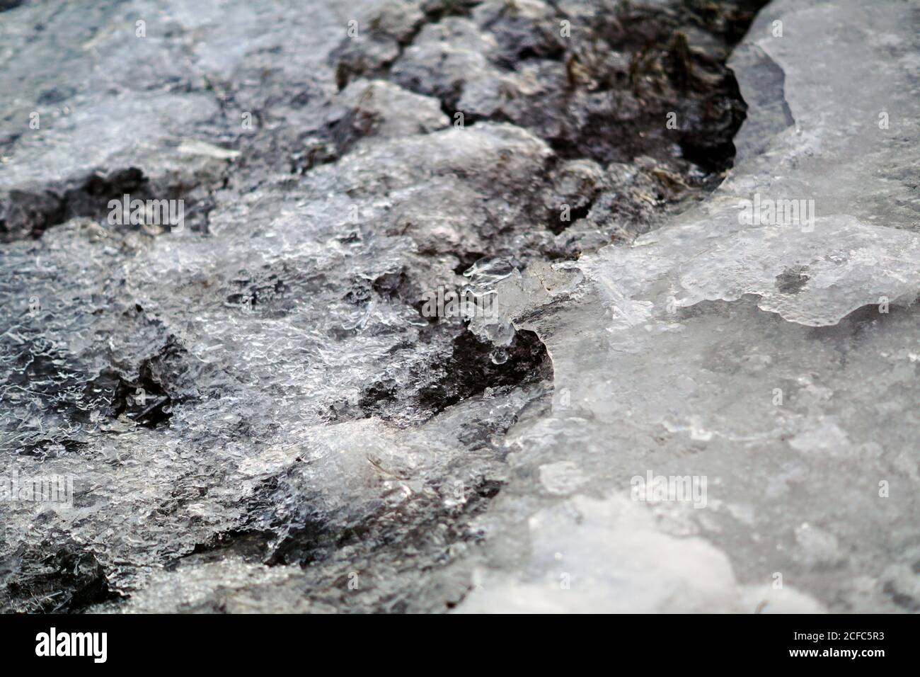 Melting ice and snow on top of rocky surface with pebbles in daylight ...