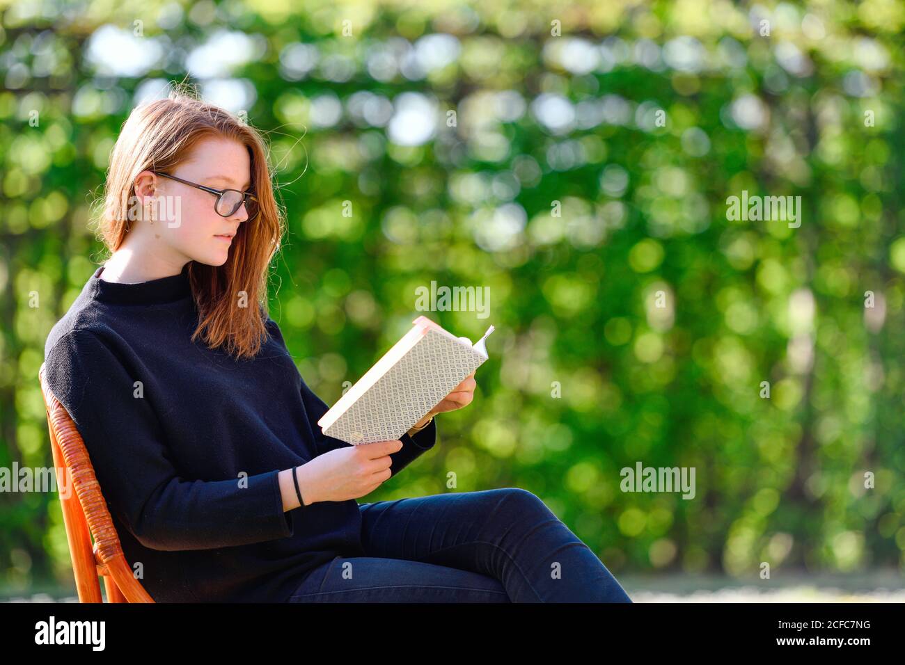 Girl sits in spring on a chair in the garden and reads in a book Stock Photo