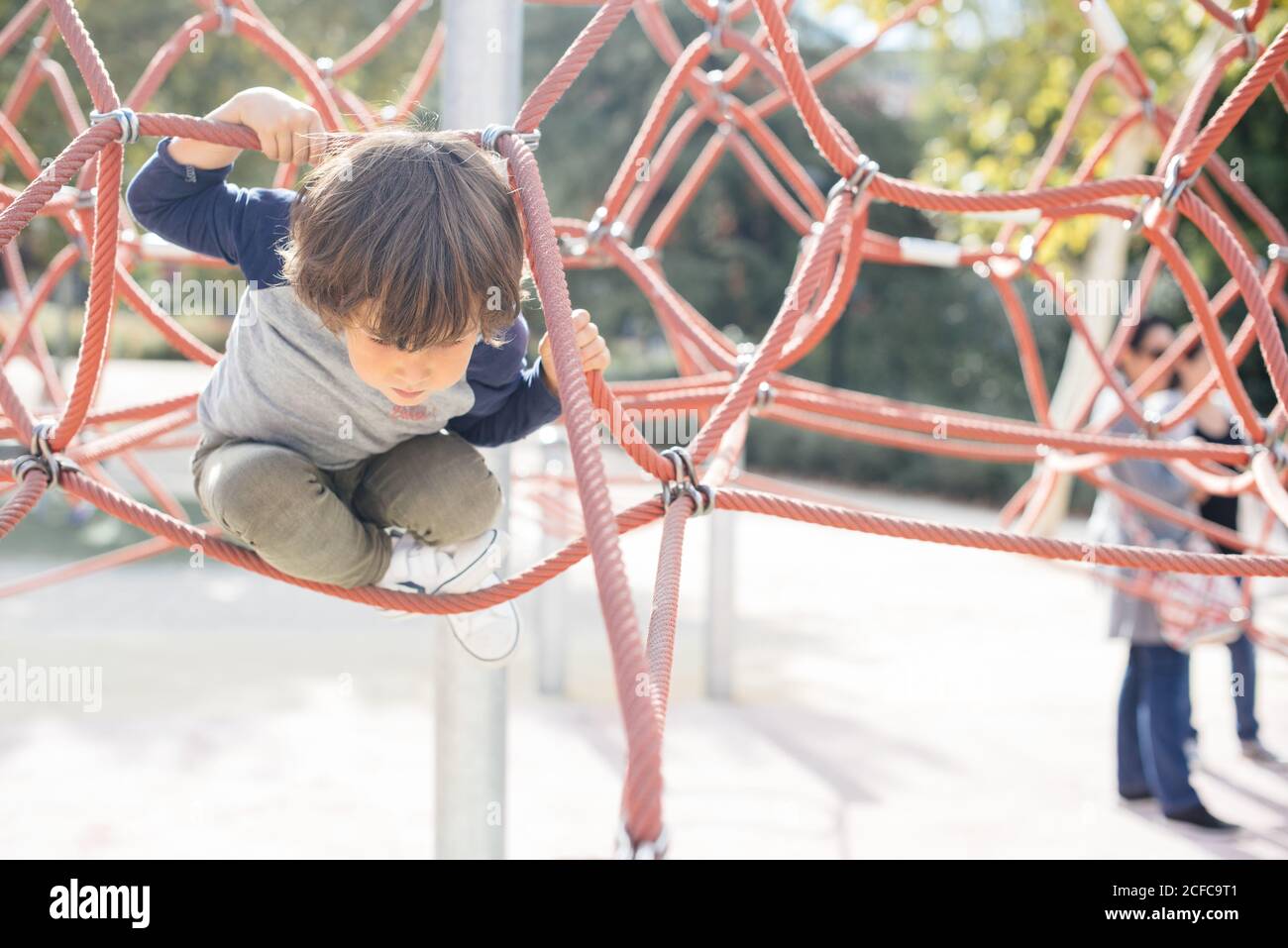 Pensive relaxed kid hanging on rope climbing net on playground in bright light Stock Photo