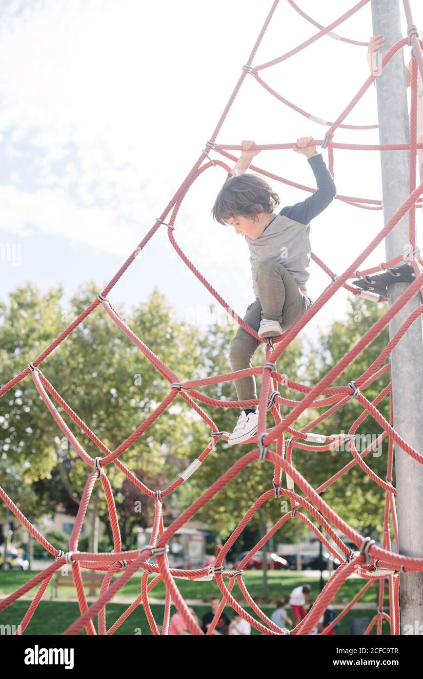 Small boy hanging on rope while walking climbing net on playground in bright light Stock Photo