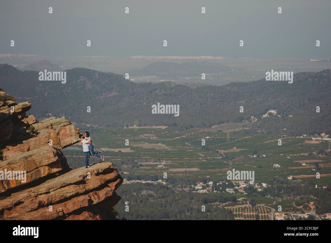 Distant loving couple embracing while standing on high cliff Stock Photo