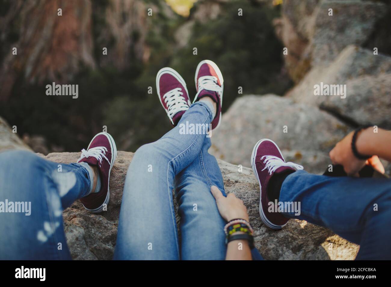 Crop from above feet relaxed couple in matching denim outfit and sneakers lying in embrace on cliff enjoying view Stock Photo