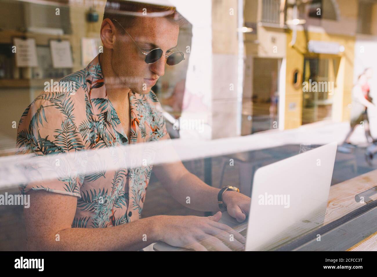 Focused young man working on laptop at table throughout a windows in coffee shop Stock Photo