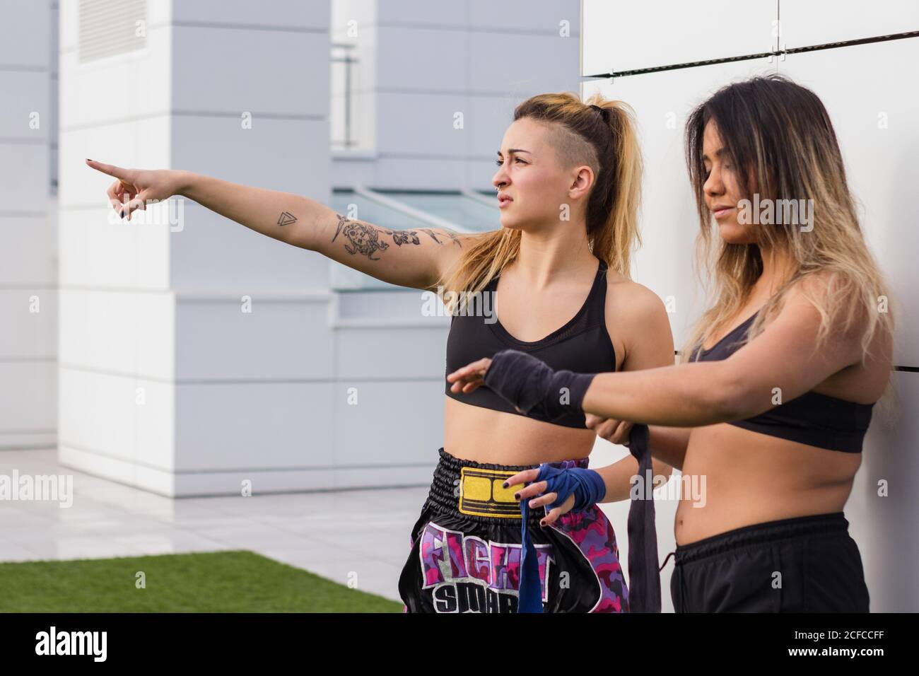 Multiethnic informal sportsWoman in active wear wrapping protective bandage on hand of female friend before training on street Stock Photo