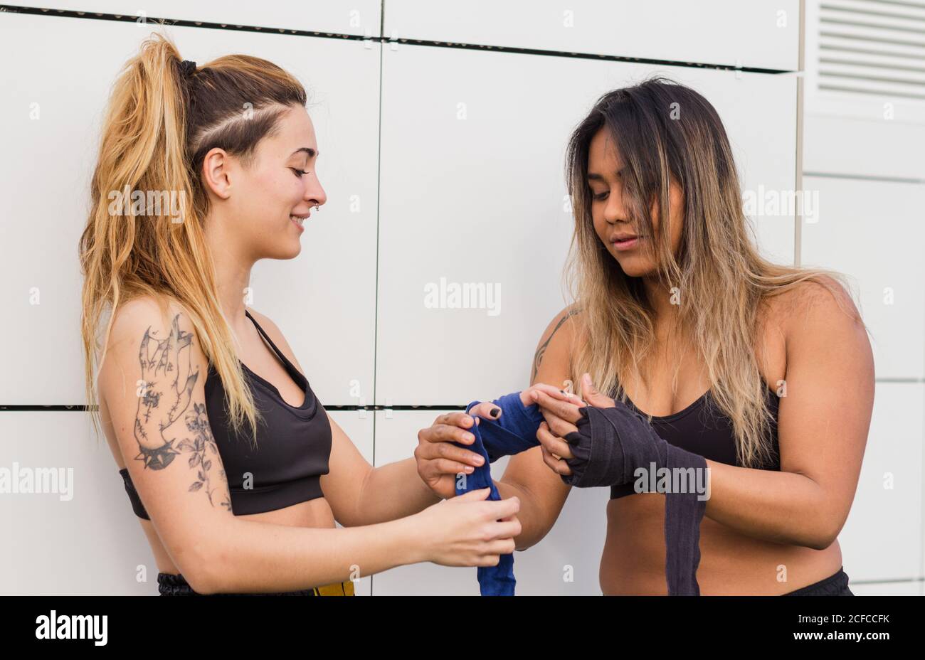 Multiethnic informal sportsWoman in active wear wrapping protective bandage on hand of female friend before training on street Stock Photo