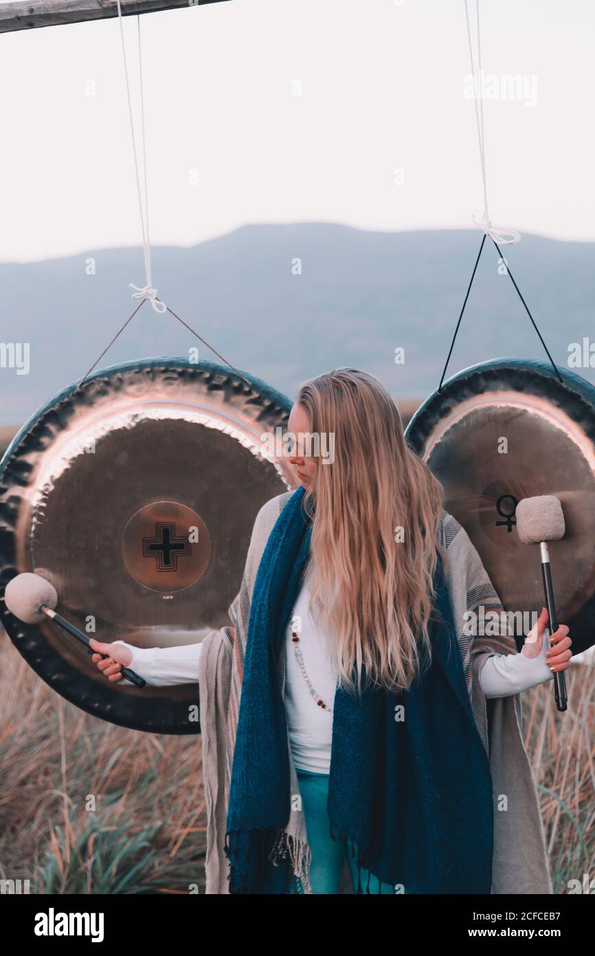 Young blond Woman with mallets near ritual gongs between lands and hills Stock Photo