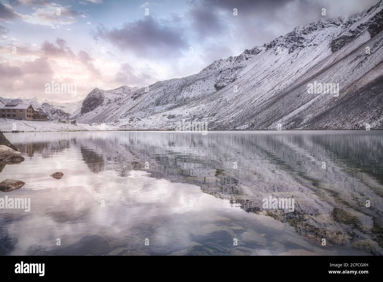 Calm lake and snowy mountain on cloudy sundown sky in Swiss National Park in Switzerland Stock Photo