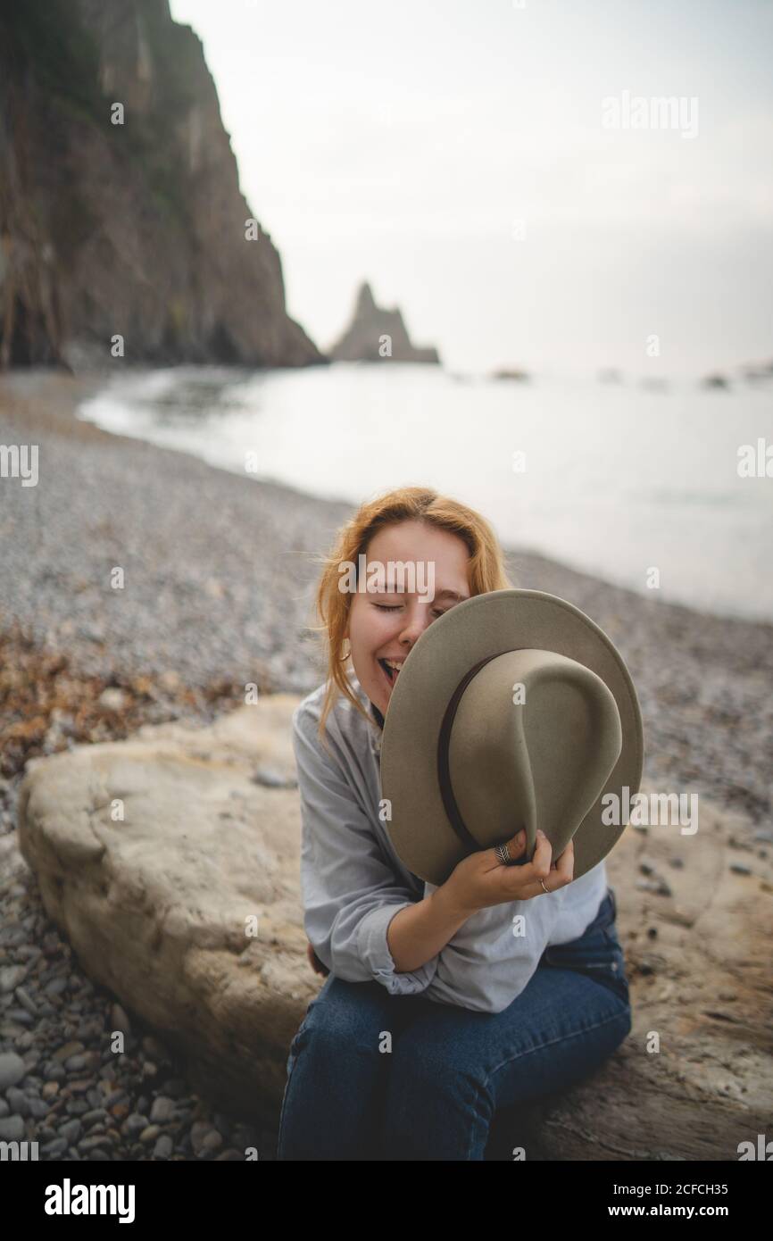 Dreaming stylish female tourist enjoying seascape while chilling on big stone on rocky shore of Asturias looking away Stock Photo