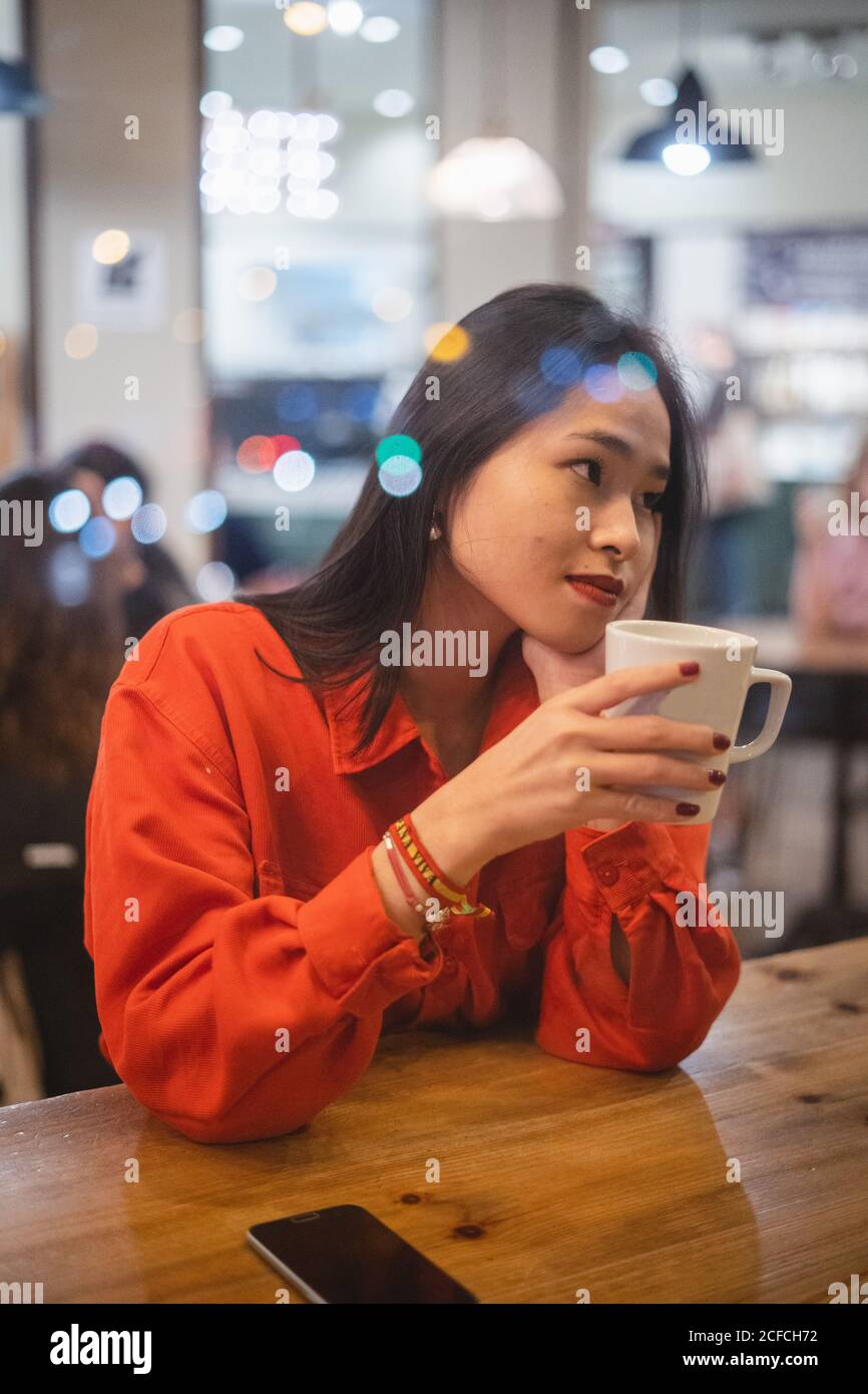 Throughout a glass view of young Woman having cup of coffee at table in cafe Stock Photo