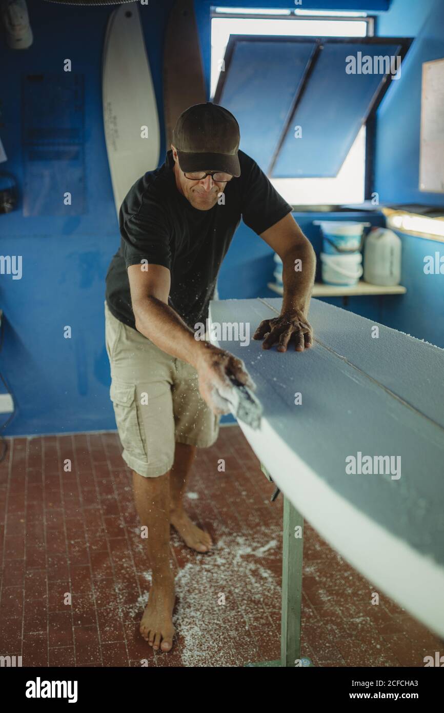 Woodworker diligently skinning surfboard in workshop Stock Photo