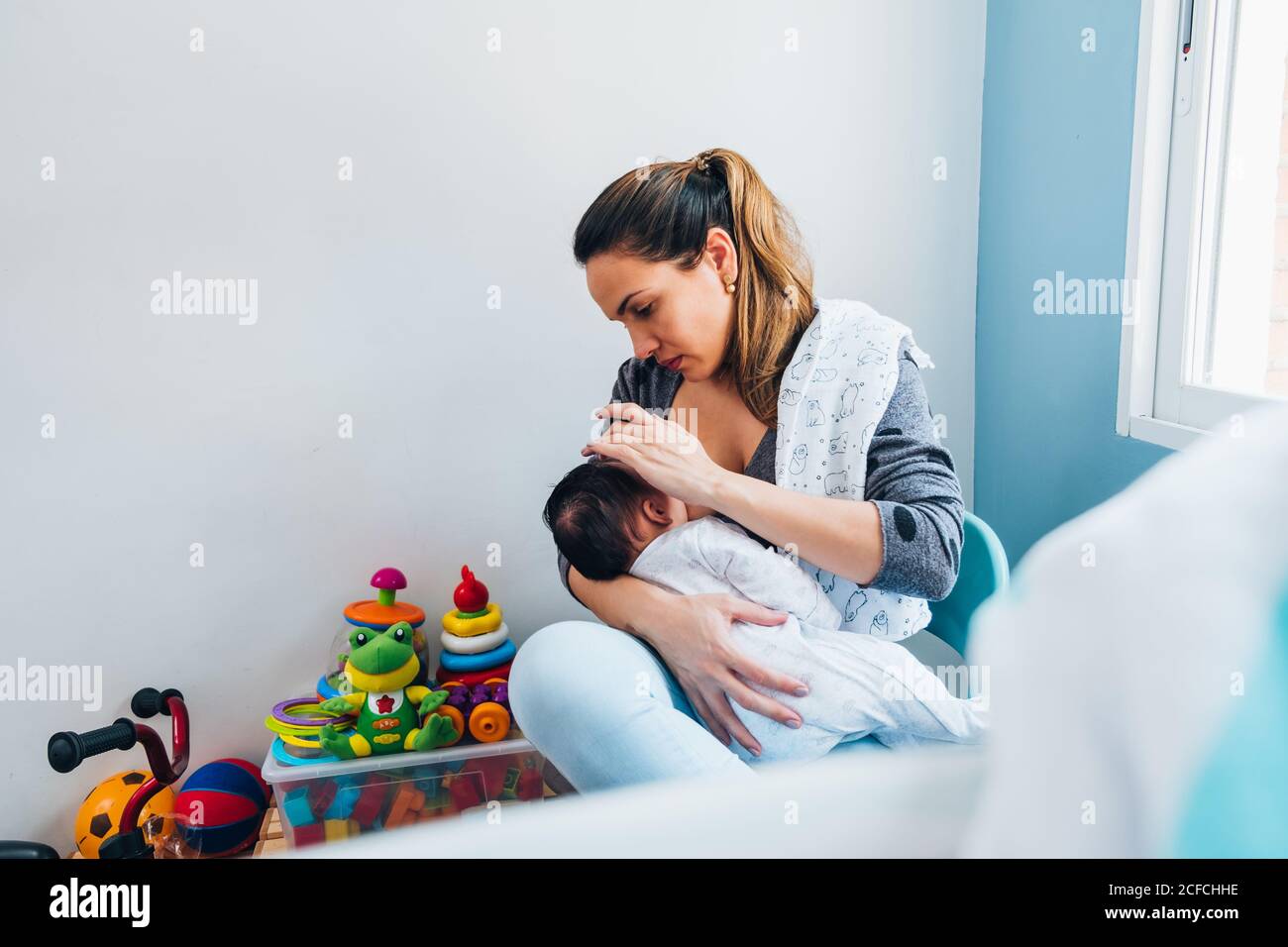 mother breastfeeding infant while sitting on chair with legs crossed