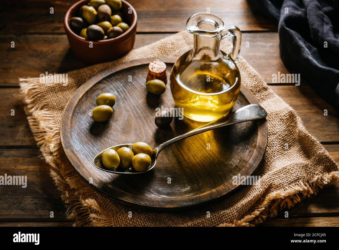 From above glass jar with extra virgin oil placed on wooden plate with black and green olives Stock Photo