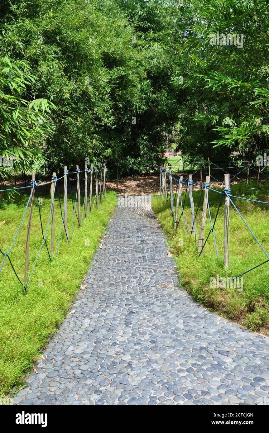 Perspective view of a cobbled stone sensory footpath made of smooth rounded pebbles, with a rustic rope fence in a rural botanical garden setting. Stock Photo