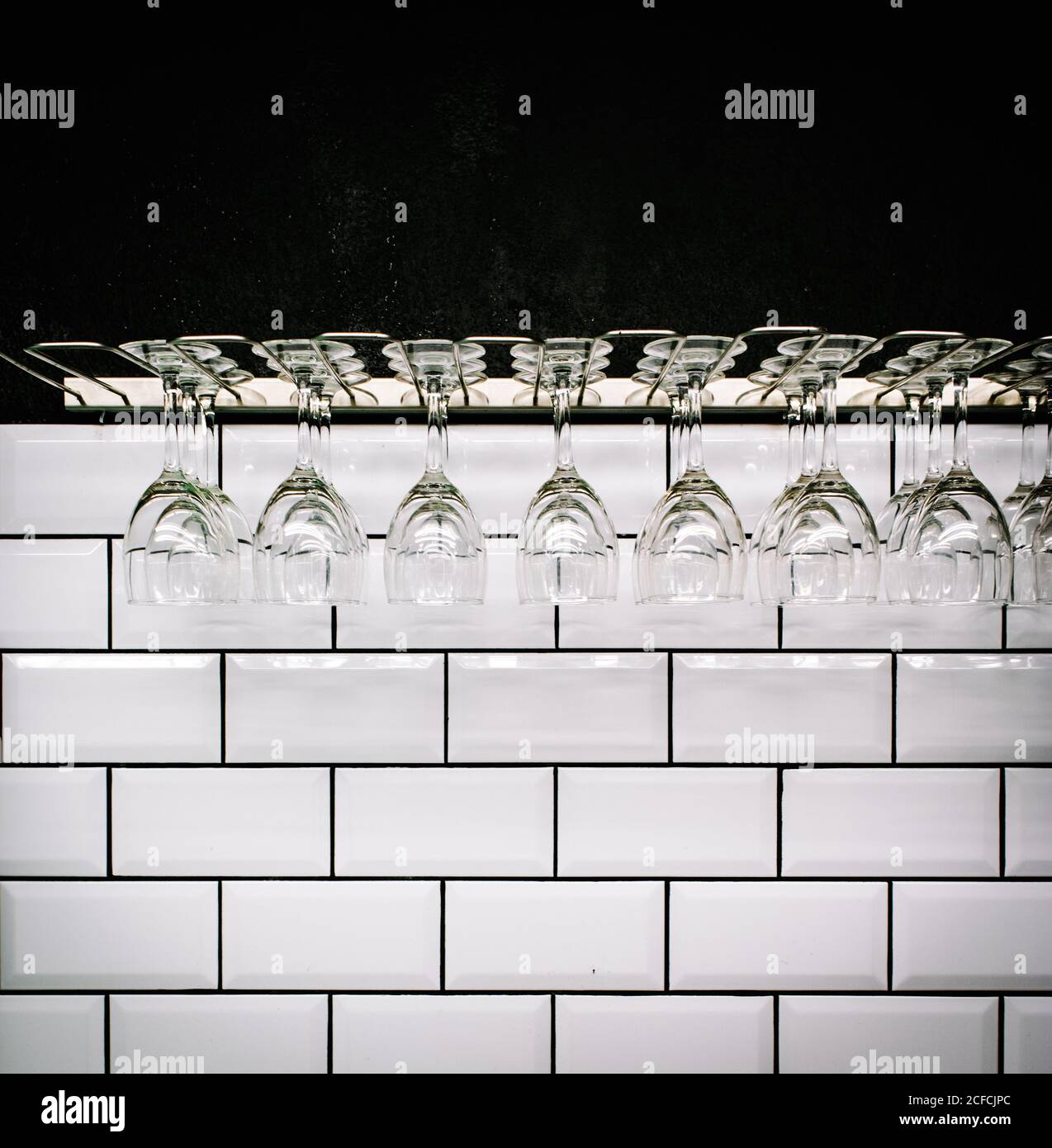 Row of clean polished wineglasses hanging against white tiled wall in vintage bar Stock Photo
