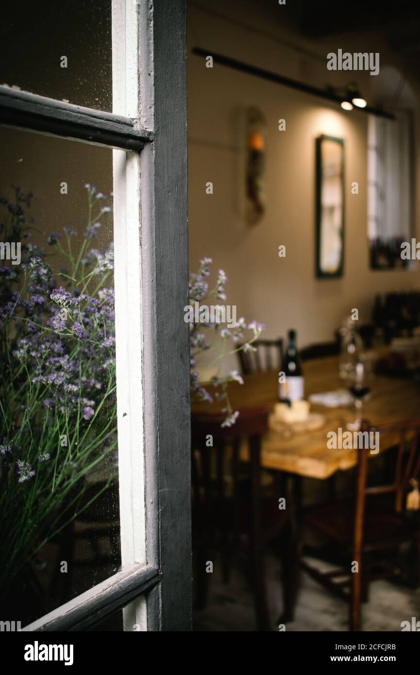 Fragment of interior of rustic restaurant with wooden table served with wine and cheese seen from open window with flowers Stock Photo