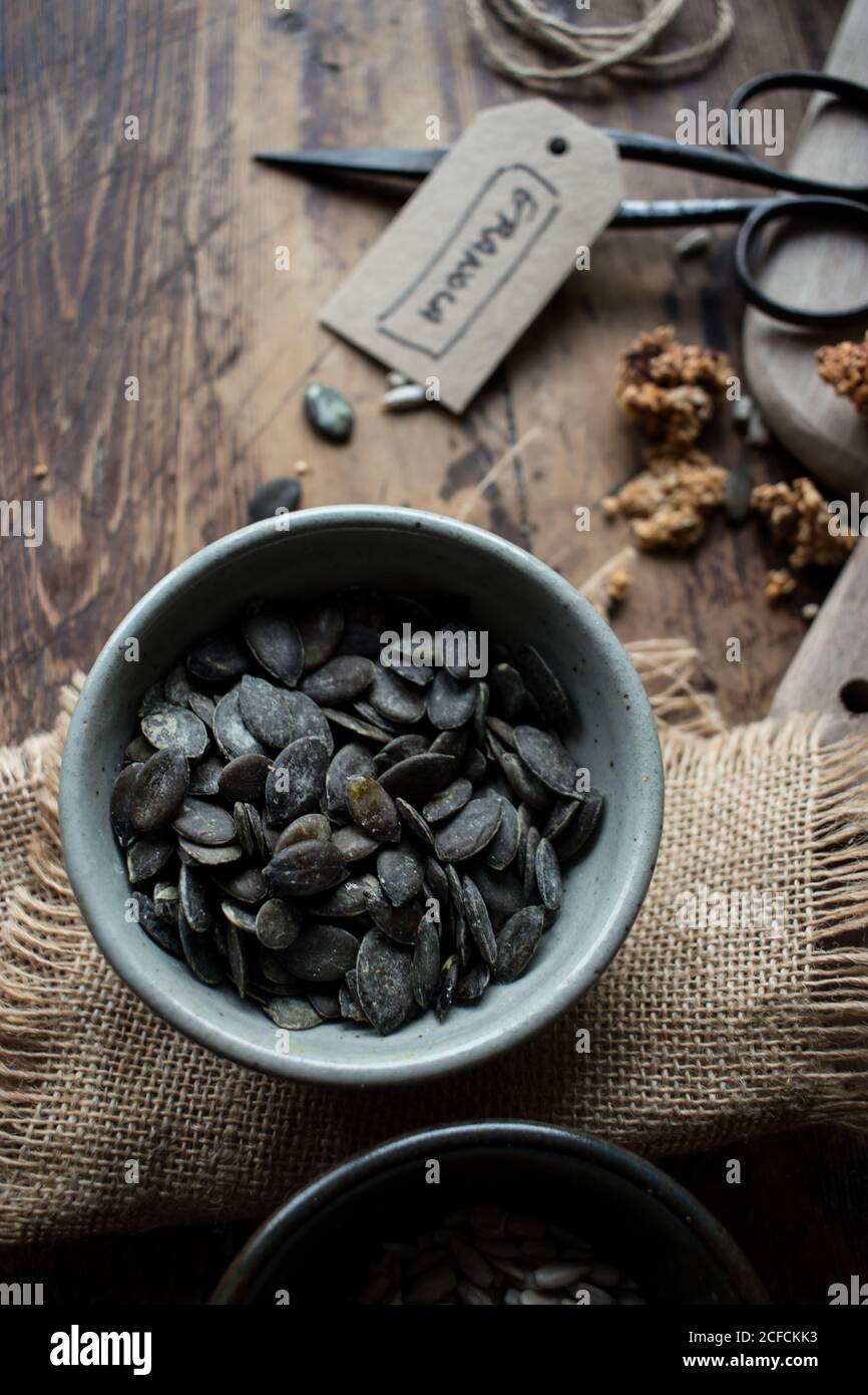 Top view of bowl of black pumpkin seeds placed on linen napkin near retro scissors and granola tag Stock Photo