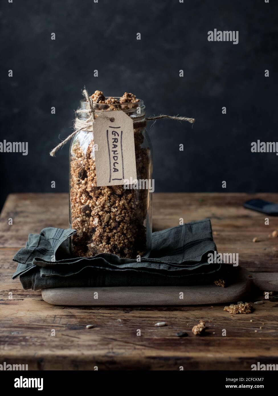 Glass jar of natural millet and quinoa granola with label placed on napkin on rustic table Stock Photo