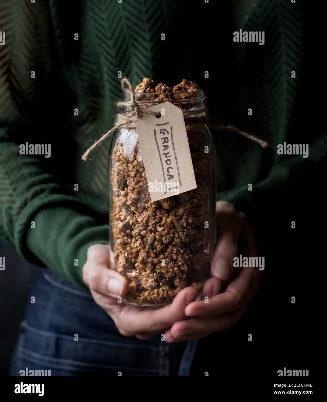unrecognizable female carrying glass jar of fresh millet and quinoa granola with label Stock Photo