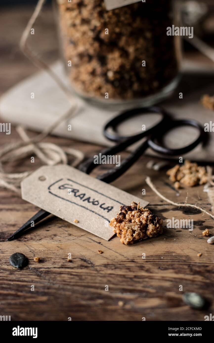 Closeup piece of fresh millet and quinoa granola placed on lumber table near vintage scissors and paper label Stock Photo