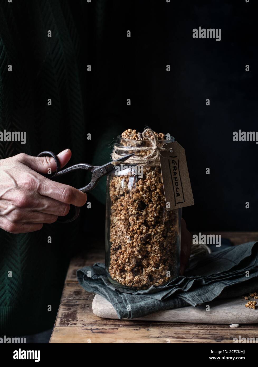 unrecognizable person using retro scissor to cut rope with label from glass jar of millet and quinoa granola Stock Photo