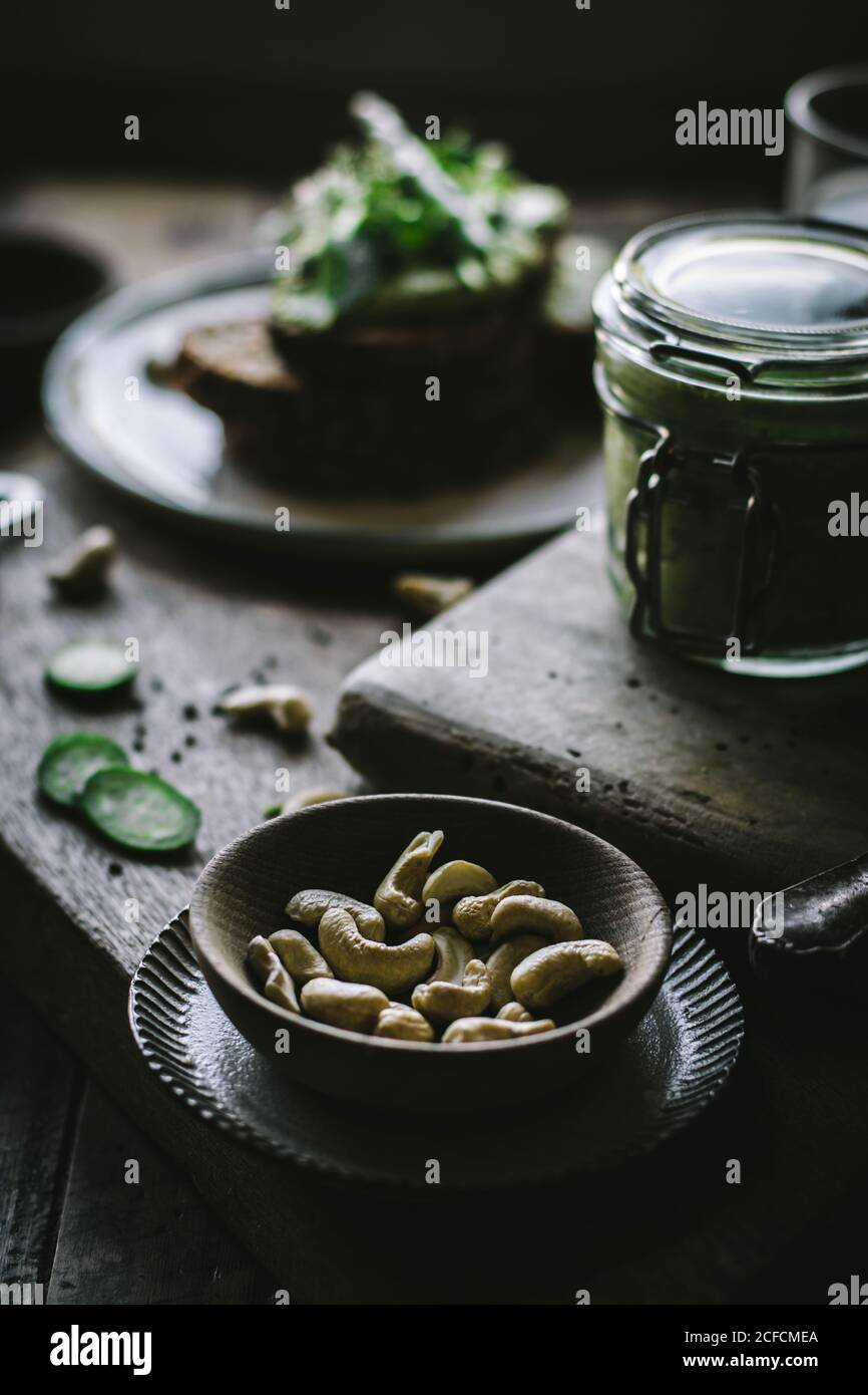 Small wooden bowl of raw cashew nuts for preparing green vegan pate on wooden board Stock Photo