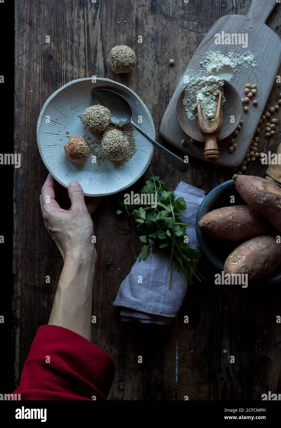 From above crop hands of person preparing sweet potatoes near tray, vegetables and parsley on wooden background Stock Photo