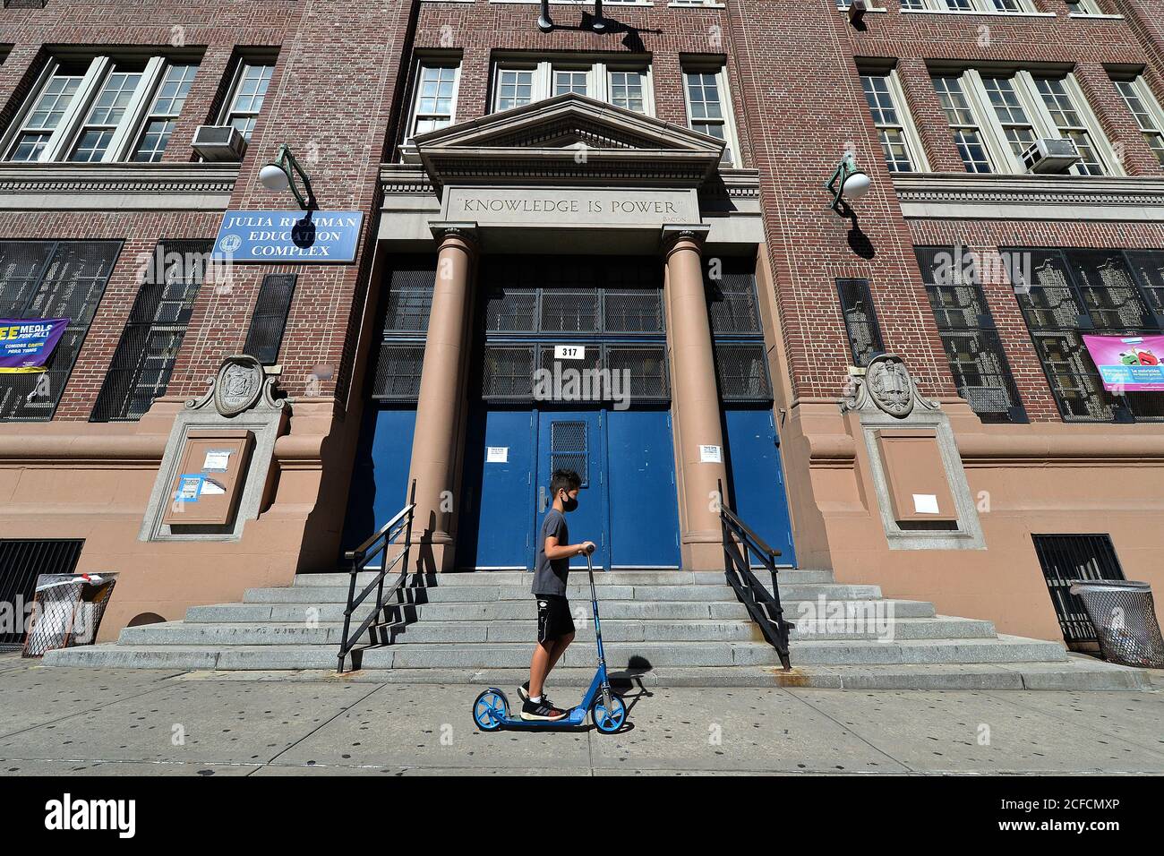A young boy rides a scooter past the entrance to the Julia Richman Education Complex High School on Manhattan's Upper East Side in New York, NY, September 4, 2020. New York City and the Department of Education are delaying the reopening of of schools until September 21, to further prepare for in-person classes for the 1.1 million children that will be going back to class; the United Federation of Teachers has said that certain health criteria, such as mandatory mask wearing, must be in place before they will re-enter classrooms. (Anthony Behar/Sipa USA) Stock Photo